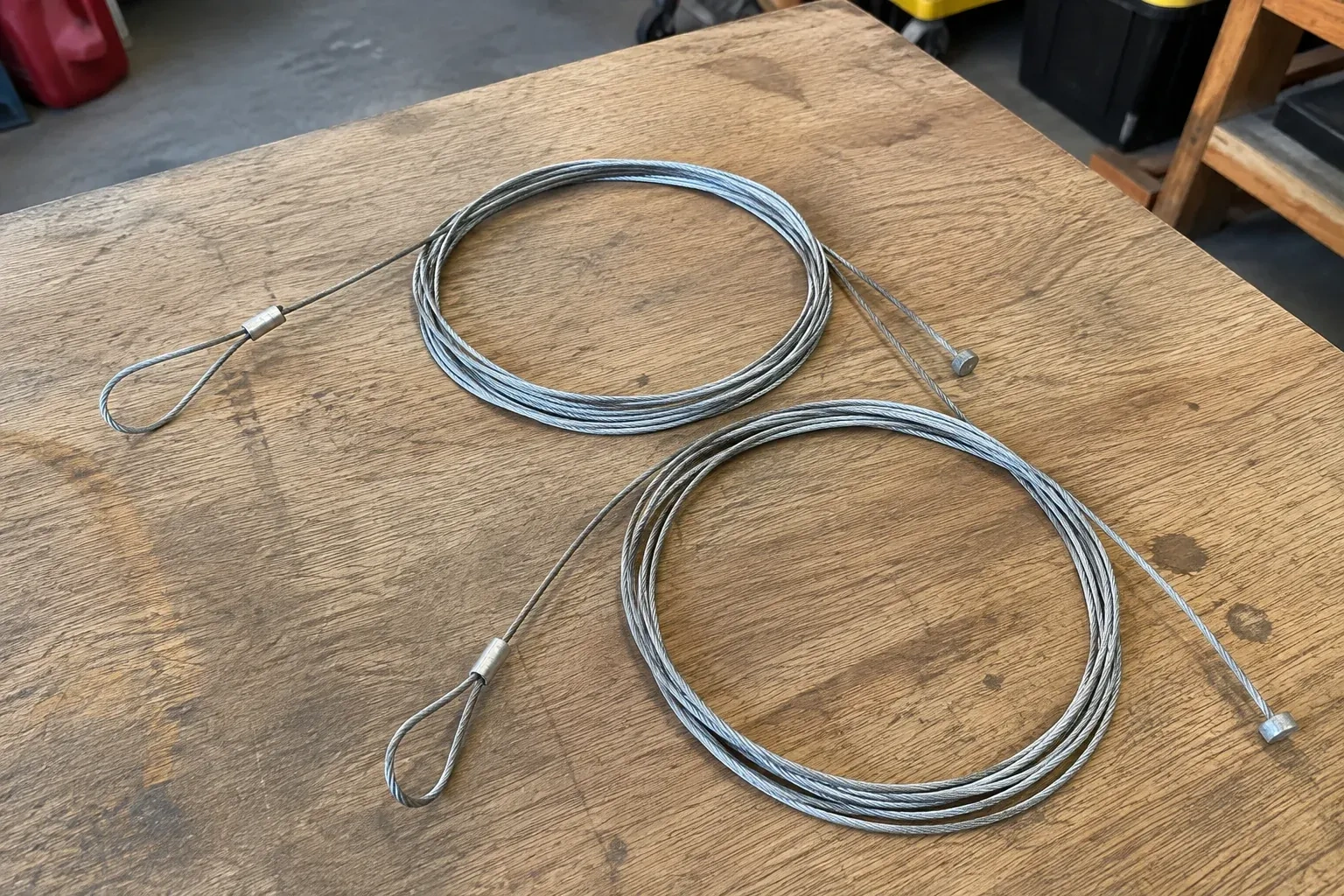 Two coiled steel cables with loop and stop ends on a workbench. — Garage Door Cable Replacement, Kitchener
